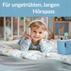 A young child wearing headphones is lying on a bed, smiling. Produktbild-Vorschau