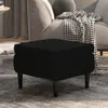 A black velvet ottoman with wooden legs sits on a gray rug in front of a sofa with a black and white patterned throw blanket. Náhľad obrázku produktu