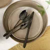 A close-up overhead view of a set of black cutlery placed on top of two plates. Náhled obrázku produktu