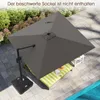 An outdoor patio scene with a large grey cantilever umbrella providing shade over a lounge chair with green and white striped cushions. A small white side table is also visible. Náhled obrázku produktu