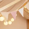 A close-up view of a decorative set for a child's bed, featuring a fabric bunting with triangular flags and a string of round LED lights. Voir les images du produit