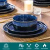 A table setting with blue stoneware plates and bowls, a candle, and gold cutlery. Produktbild-Vorschau
