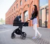 A woman is pushing a stroller on a brick-paved sidewalk in front of a brick building. Náhled obrázku produktu