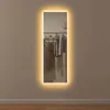 A full-length mirror with LED lighting is mounted on a wall, reflecting clothes hanging on a rack. Produktbild-Vorschau