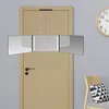 A tri-fold mirror with LED lights hangs on a wooden door, with a clock and chair visible in the background. Produktbild-Vorschau