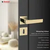 A close-up of a gold-colored door handle and lock escutcheon on a dark door, with a blurred interior scene in the background. Produktbild-Vorschau