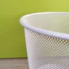 A close-up of the top rim of a white wire mesh trash can against a lime green background. Produktbild-Vorschau