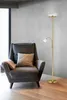 A floor lamp with a reading light is placed next to an armchair in a room with a concrete wall and wooden floor. Produktbild-Vorschau