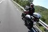 A person riding a motorcycle on a road with a scenic background. Produktbild-Vorschau