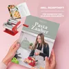 A hands-on demonstration of a pasta maker with a recipe book, likely for an advertisement. Produktbild-Vorschau