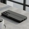 A black flip cover case for a smartphone is placed on a textured gray surface, with a white coffee cup in the foreground. Podgląd zdjęcia produktu