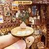 A close-up of a miniature DIY book nook, showing a small table with a vase of greenery and envelopes. Voir les images du produit