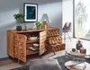 A modern living room scene featuring a wooden sideboard with open doors and drawers, displaying decorative items and tableware. A chair and coffee table are also visible. Náhled obrázku produktu