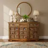 A decorated wooden sideboard with a round mirror above it, flanked by two lamps and decorative items. Produktbild-Vorschau