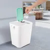 A person is throwing trash into a dual-compartment trash can in a room. Produktbild-Vorschau