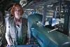 A woman with red hair stands in a room with scientific equipment. Produktbild-Vorschau