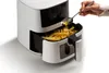 A hand is pouring oil from a spoon into an air fryer filled with french fries. Anteprima dell’immagine prodotto