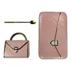 A pink handbag-shaped dish, a matching rectangular dish, and a gold spoon are arranged on a white background. Produktbild-Vorschau