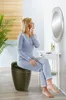 A woman applies makeup while sitting on a stool in a bathroom. Produktbild-Vorschau