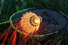 A badminton shuttlecock with a light inside is resting on a badminton racket, which is placed on grass. Produktbild-Vorschau