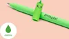 A green pen with a cartoon dinosaur cap is shown on a light pink background, with a green droplet icon and the word 'GREEN' in the bottom left corner. Náhľad obrázku produktu