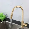 A gold kitchen faucet with water running into a stainless steel sink, with green apples in a basket in the background. Náhled obrázku produktu