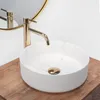 A white round vessel sink with marble-like veining and a gold drain is placed on a wooden countertop. Produktbild-Vorschau