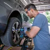 A mechanic is using a cordless impact wrench to remove a car wheel while the car is lifted on a hydraulic lift. Voir les images du produit