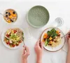 A top-down view of a table setting with multiple healthy meals and a green colander. Anteprima dell’immagine prodotto
