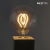 A close-up shot of a vintage-style LED light bulb with a heart-shaped filament, mounted on a black and wood base. Produktbild-Vorschau