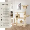 A multi-level cat tree with various platforms, a hammock, a hideaway, and scratching posts, set in a well-lit room with a sofa and artwork in the background. Náhled obrázku produktu