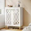A white shoe cabinet with mirrored doors and gold legs, placed in a room next to a window and a bed. Produktbild-Vorschau