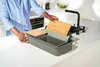 A person is placing a cutting board into a sink accessory. Voir les images du produit