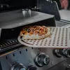 A pizza is being placed into a grill oven using a pizza peel. Podgląd zdjęcia produktu