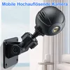 A small black security camera mounted on a wall bracket, with a blurred background of curtains and furniture. Produktbild-Vorschau