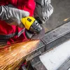 A person wearing protective gloves and a red jacket is using a yellow angle grinder to cut a metal beam, creating a shower of sparks. Produktbild-Vorschau