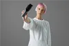 A woman with pink hair holds a black hair clipper in front of a gray background. Podgląd zdjęcia produktu