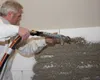 A man is applying plaster to a wall using a spray gun. Produktbild-Vorschau