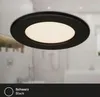 A black LED ceiling light with a white illuminated center, shown in a blurred bathroom setting. Produktbild-Vorschau