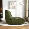 A green bean bag chair is placed on a rug in a well-lit living room, with a floor lamp and artwork on the wall. Produktbild-Vorschau