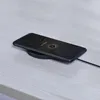 A black smartphone is placed on a black wireless charging pad on a light gray wooden surface. Produktbild-Vorschau