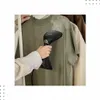 A person is steaming a green t-shirt with a handheld garment steamer. Podgląd zdjęcia produktu