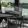 An outdoor dining set with a round table and chairs, set against a backdrop of a building with large windows. Produktbild-Vorschau