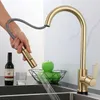 A hand is holding a gold kitchen faucet spray head, with water spraying out into a sink. A bottle of wine, a glass, and a bowl of green apples are on the counter. Produktbild-Vorschau