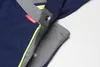 A close-up view of a navy blue work garment with gray accents and a yellow stripe, showing snap closures and a brand label. Produktbild-Vorschau