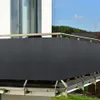 A dark grey privacy screen is attached to a balcony railing, with a house and trees in the background. Produktbild-Vorschau