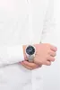 A person wearing a white shirt and a silver watch with a black face. Voir les images du produit