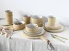 A collection of ceramic tableware, including cups, bowls, and plates, arranged on a white tablecloth with a wooden board. Produktbild-Vorschau