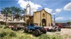 Several off-road vehicles are parked in front of a church and a building with graffiti. Produktbild-Vorschau