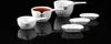 A set of white ceramic dipping bowls and sauce boats are arranged on a reflective black surface. Náhľad obrázku produktu